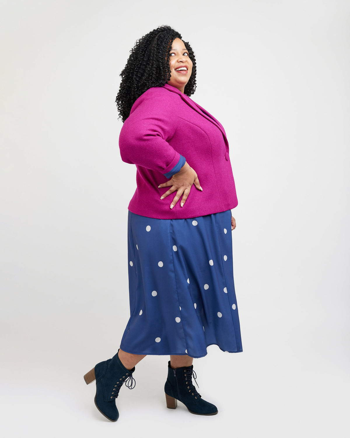 Woman wearing a pink jacket and blue polka dot skirt on a white background. This blazer is the Auburn Blazer sewing pattern from Cashmerette.