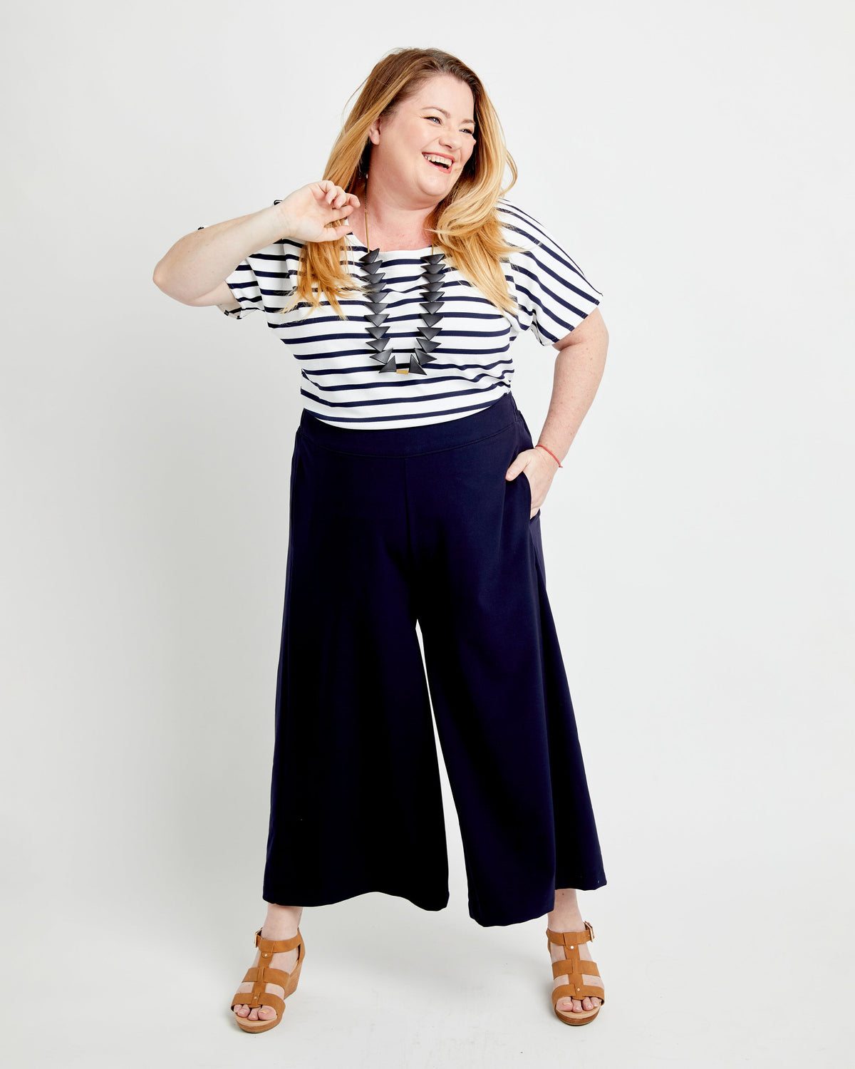 Woman wearing a striped shirt and navy wide-leg pants on a white background. These pants are the Calder Pants & Shorts sewing pattern from Cashmerette.