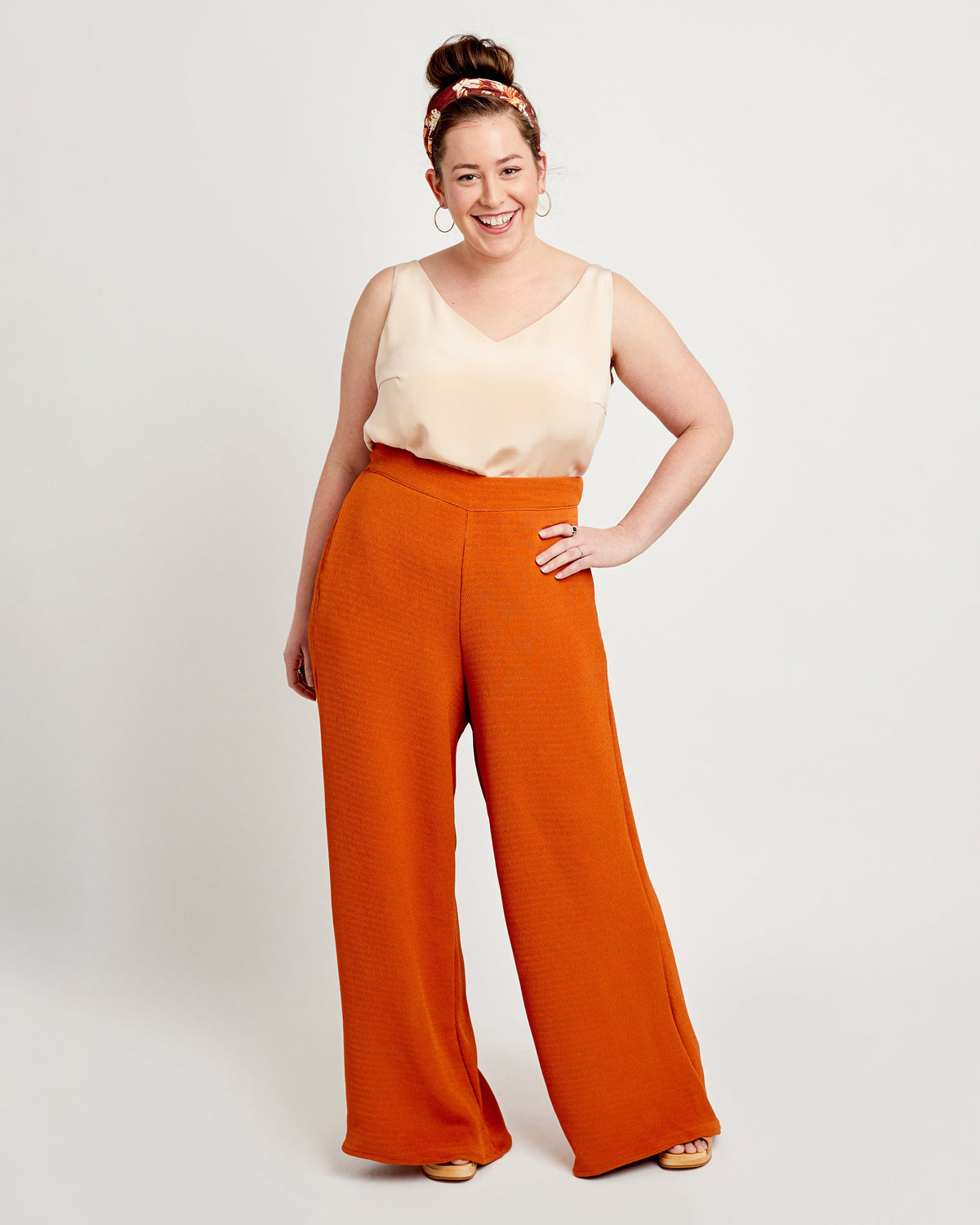 Woman wearing a cream top and orange wide-leg pants on a white background. These pants are the Calder Pants & Shorts sewing pattern from Cashmerette.