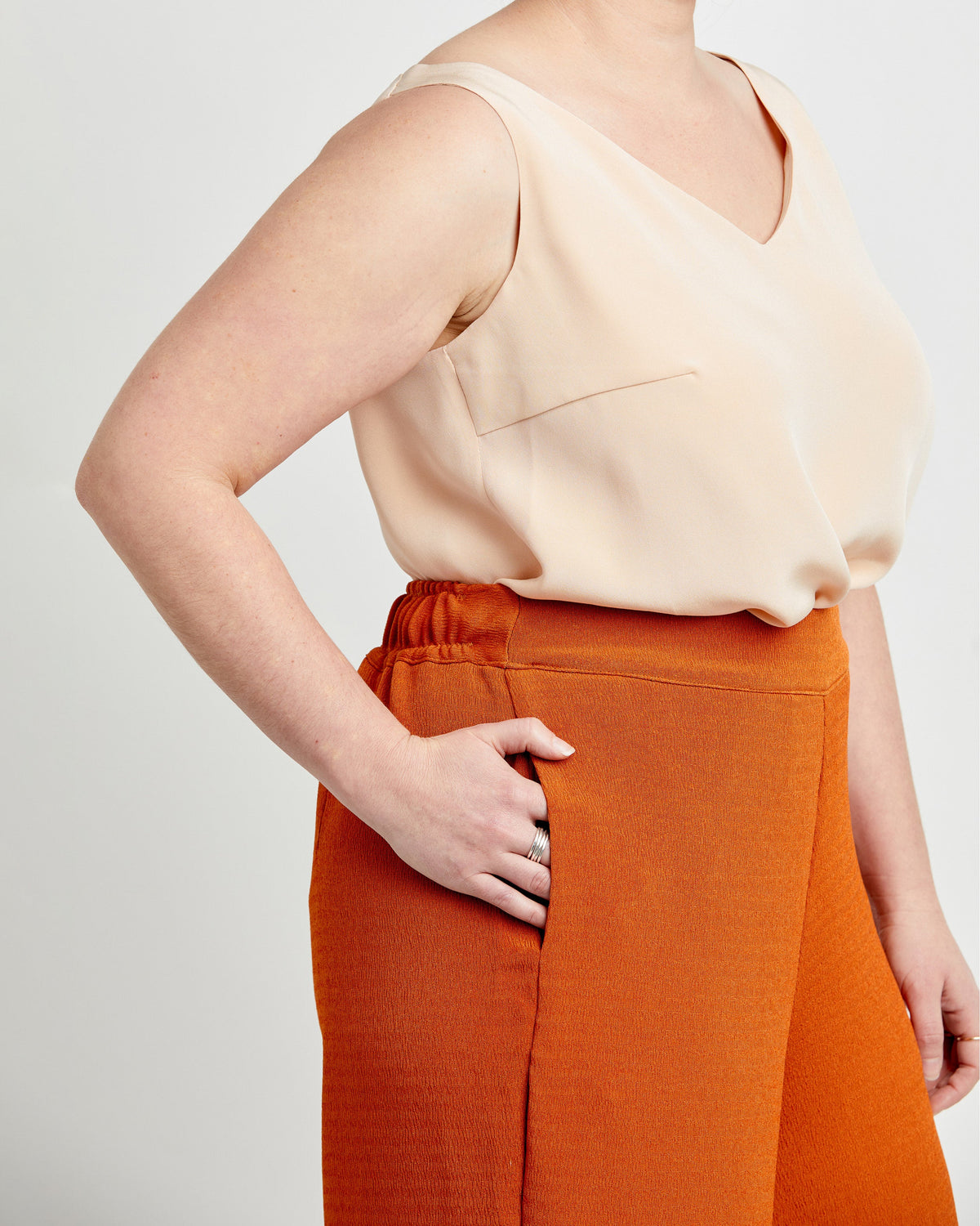 Person wearing a beige top and orange pants on a plain background. These pants are the Calder Pants & Shorts sewing pattern from Cashmerette.