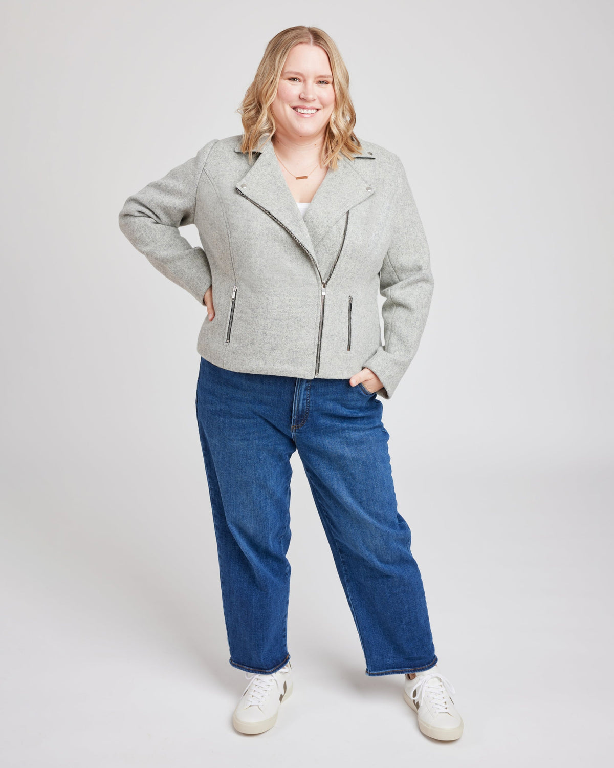 Woman wearing a gray jacket and blue jeans on a white background. This biker jacket is the Canton Moto Jacket sewing pattern from Cashmerette.