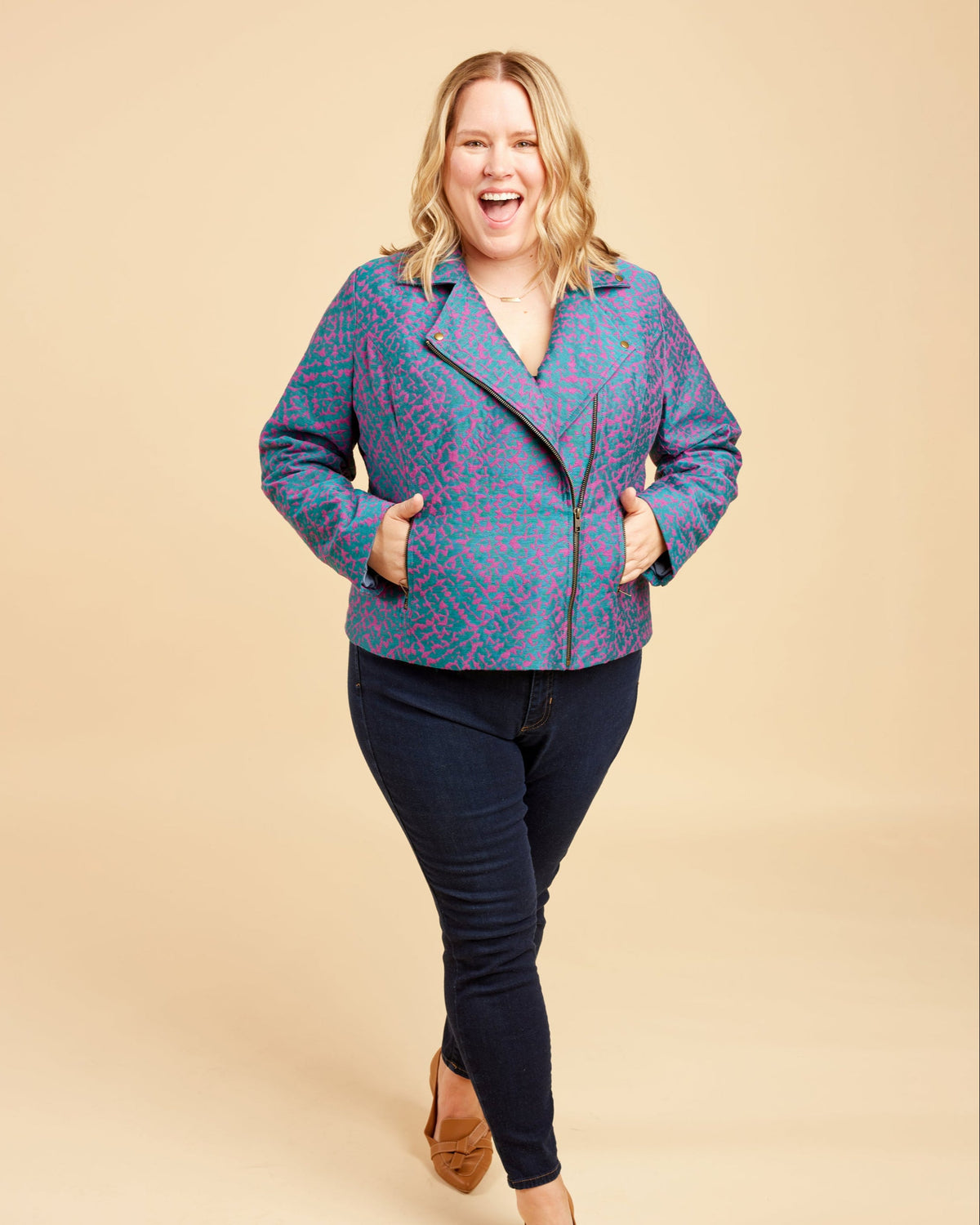 Woman wearing a blue patterned jacket and black pants on a beige background. This biker jacket is the Canton Moto Jacket sewing pattern from Cashmerette.