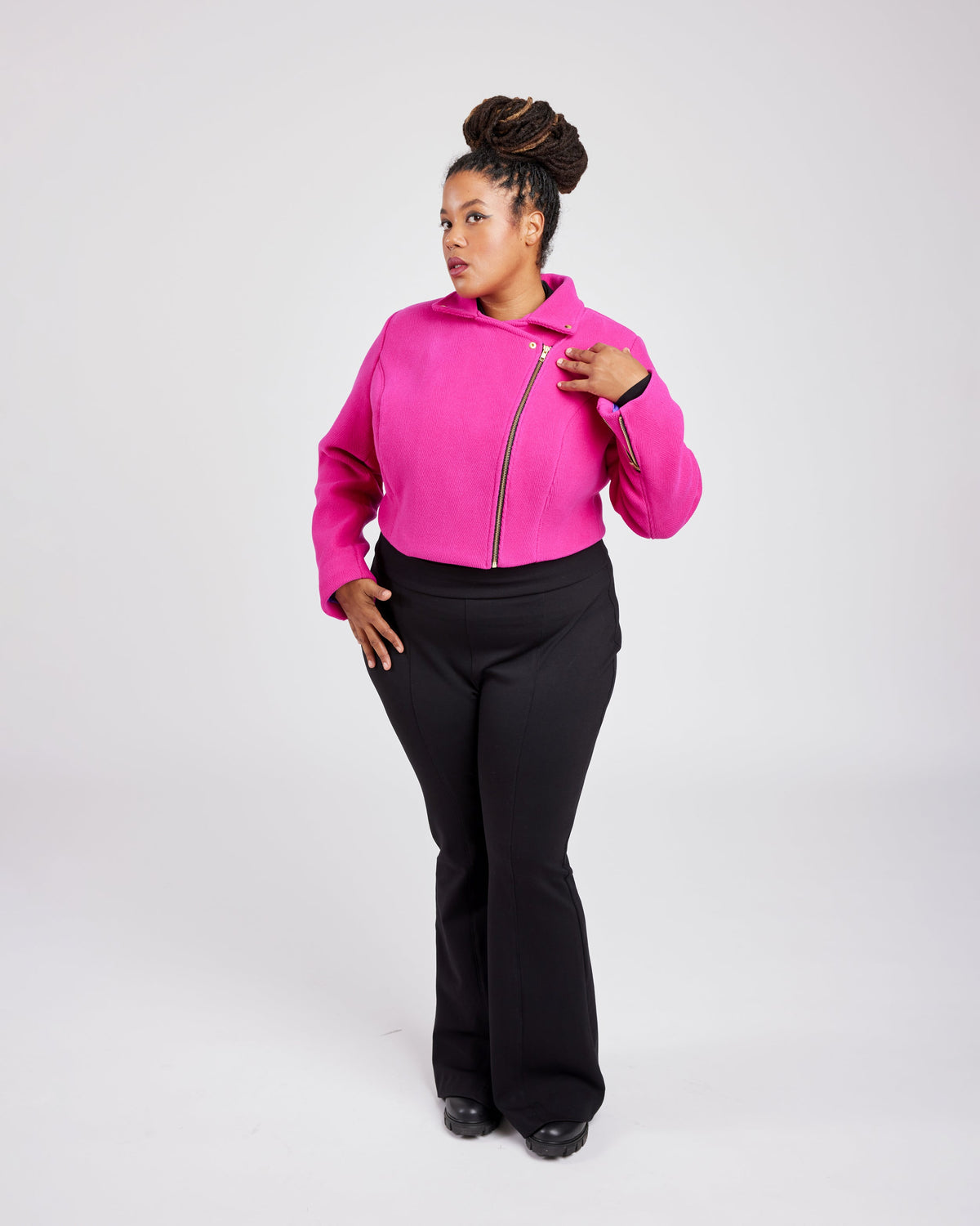 Person wearing a bright pink hoodie with a zipper and black pants on a white background. This biker jacket is the Canton Moto Jacket sewing pattern from Cashmerette.