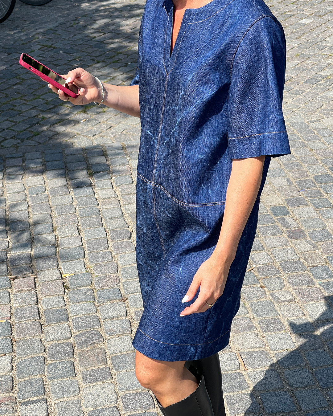 Person wearing a blue denim dress on a cobblestone street.