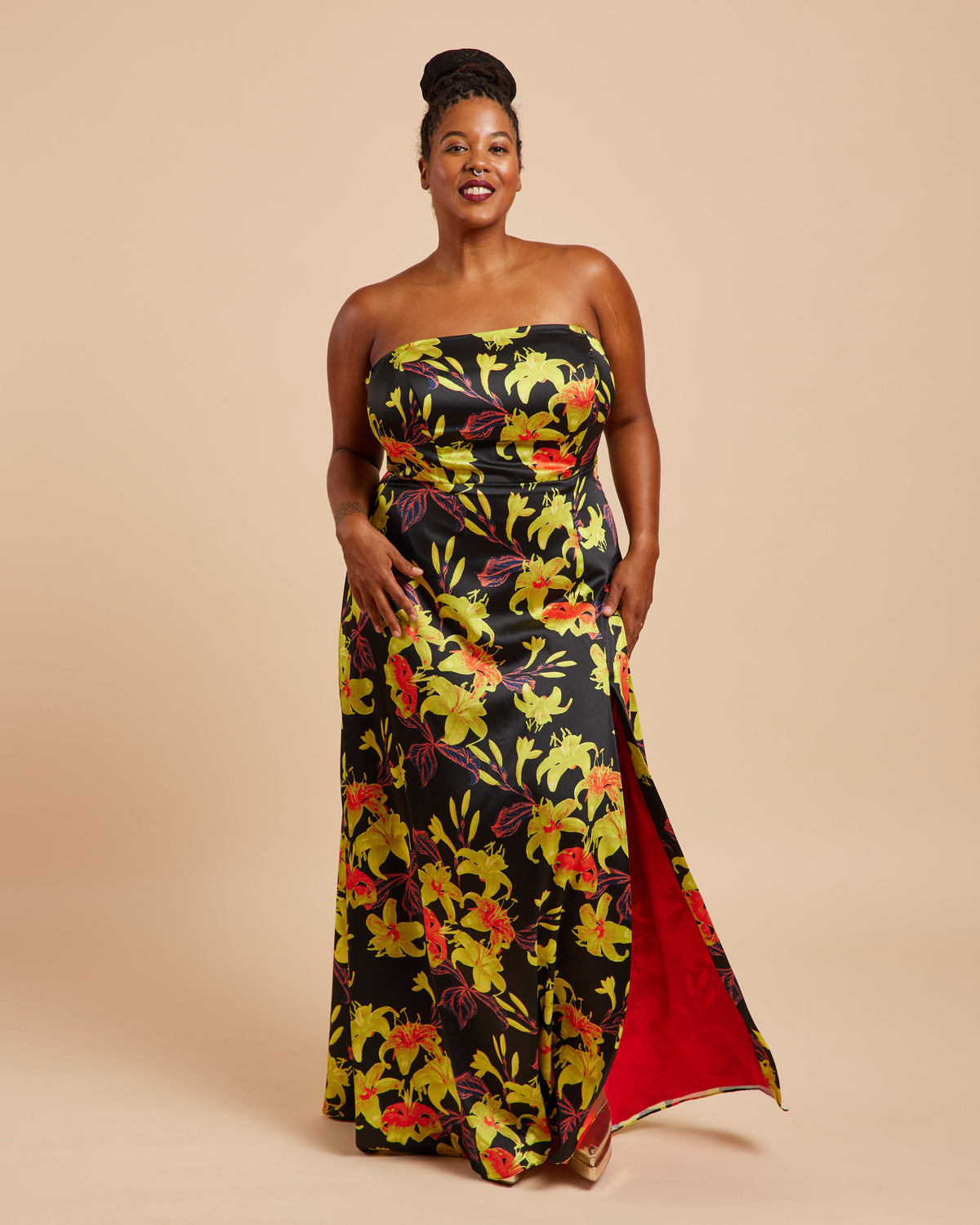 Woman wearing a strapless floral dress with a red lining on a beige background. This dress is the Ellington Strapless Dress sewing pattern from Cashmerette.
