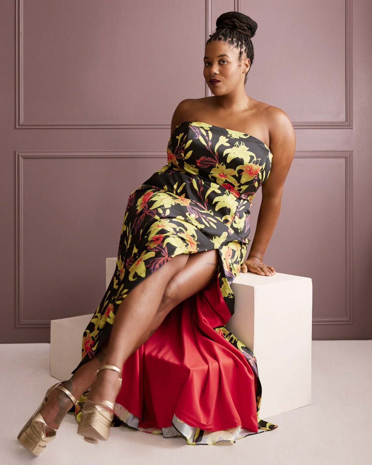 Woman in a floral strapless dress sitting on a white cube against a purple wall. This dress is the Ellington Strapless Dress sewing pattern from Cashmerette.