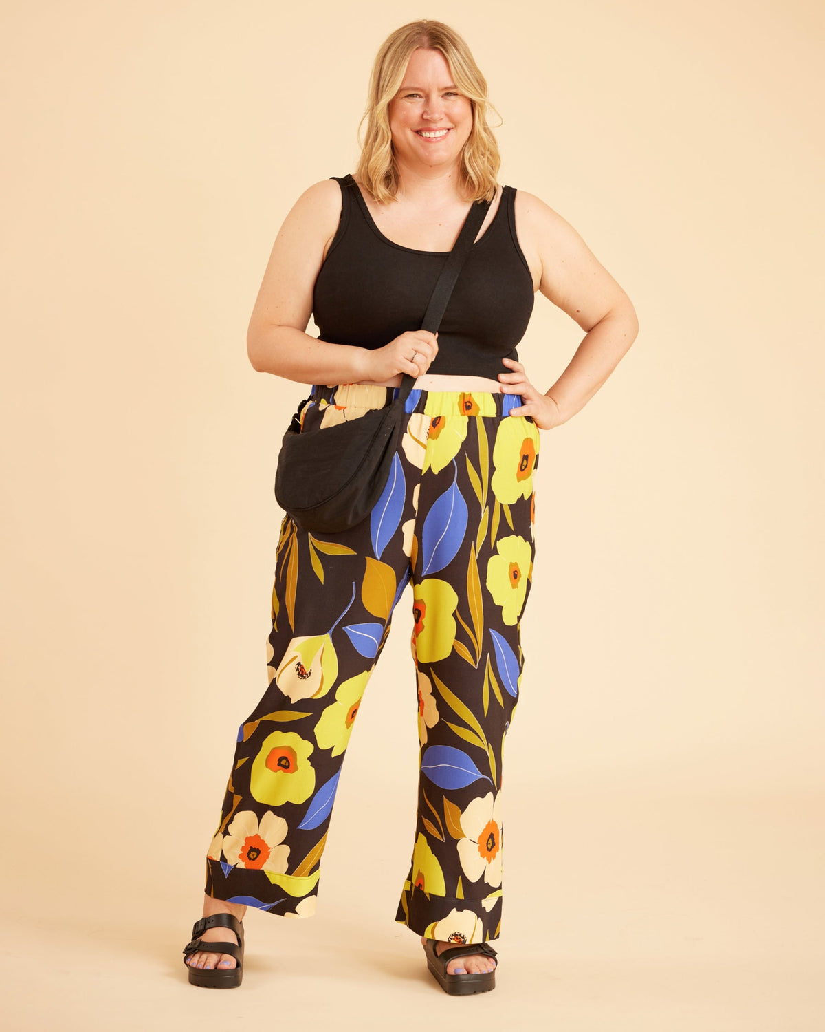 Woman wearing a black tank top and floral pants against a beige background. This is the Fiske Sleepwear Set sewing pattern from Cashmerette.