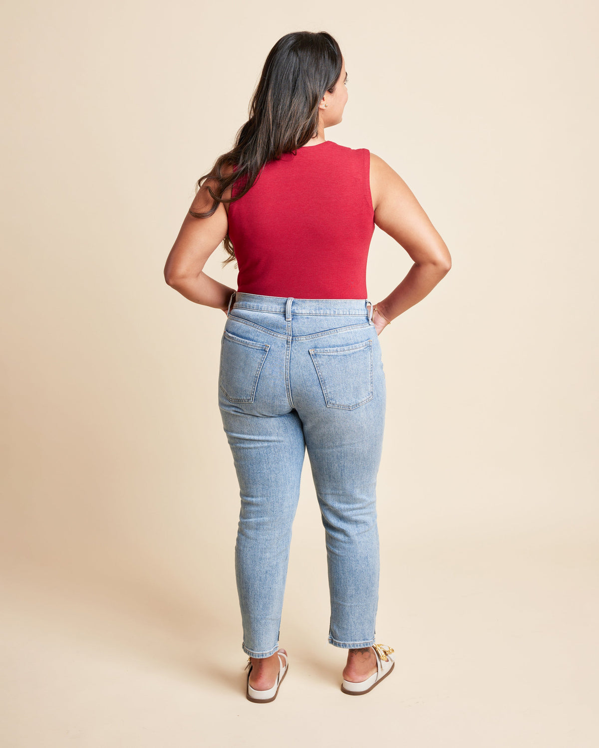 Woman wearing a red sleeveless top and light blue jeans on a beige background. This is the Grafton Dress, Top & Skirt sewing pattern from Cashmrette.