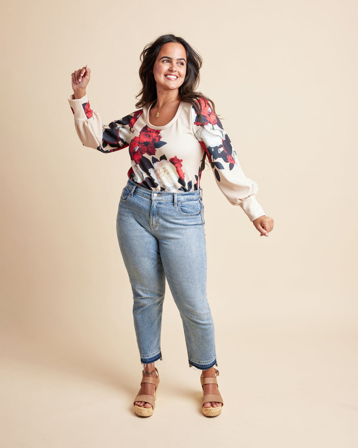 Woman wearing a floral blouse and jeans on a beige background. This is the Grafton Dress, Top & Skirt sewing pattern from Cashmrette.