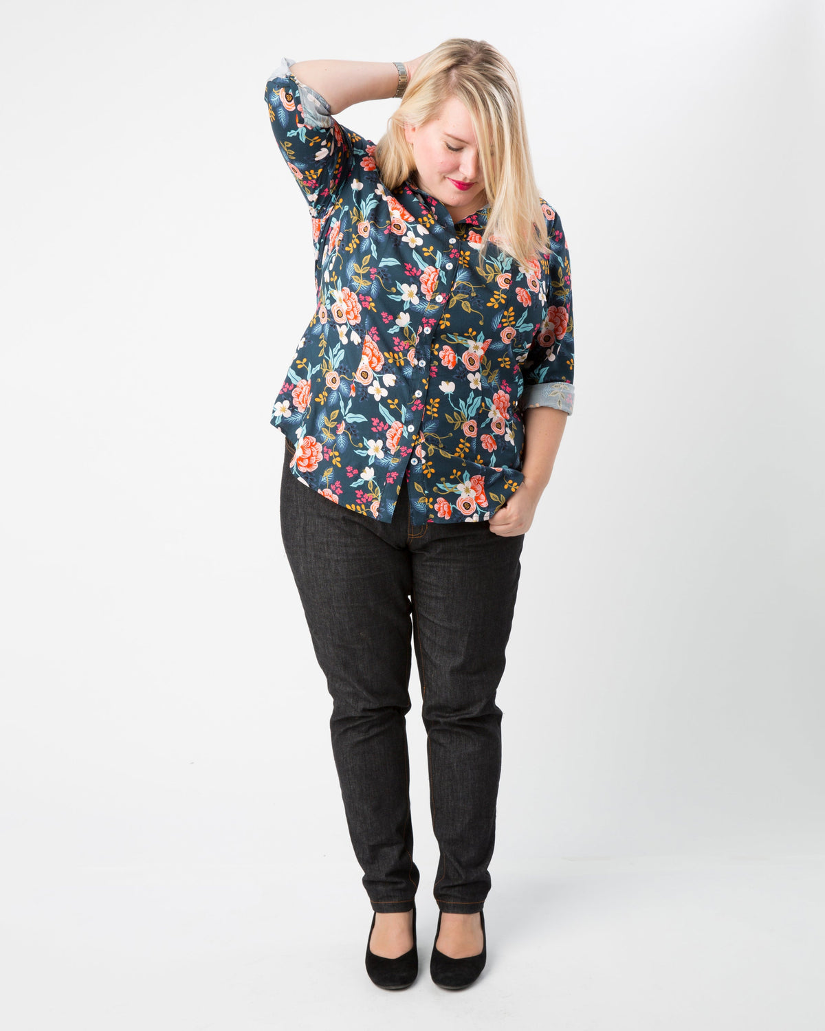 Woman wearing a floral blouse and black pants on a white background. This button-up shirt is the Harrison Shirt sewing pattern from Cashmerette.
