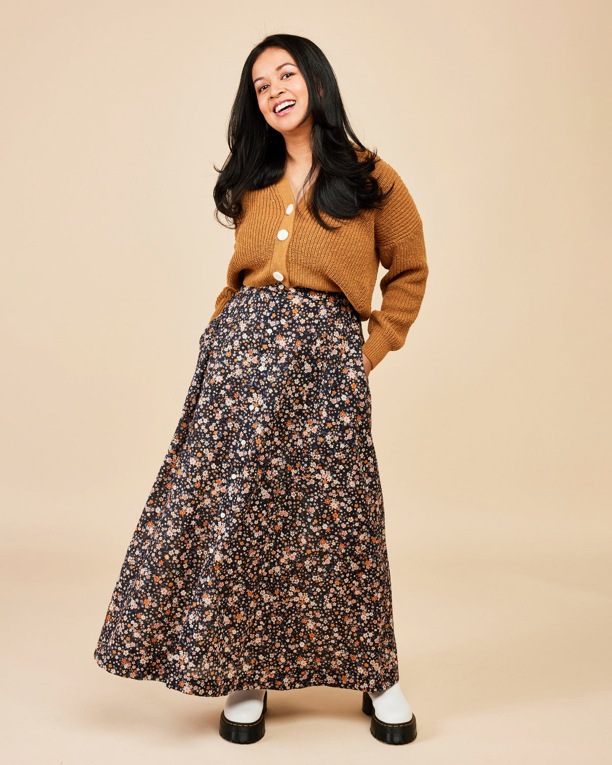 Woman wearing a mustard yellow cardigan and floral skirt on a beige background. This is the Holyoke Maxi Dress & Skirt sewing pattern from Cashmerette.