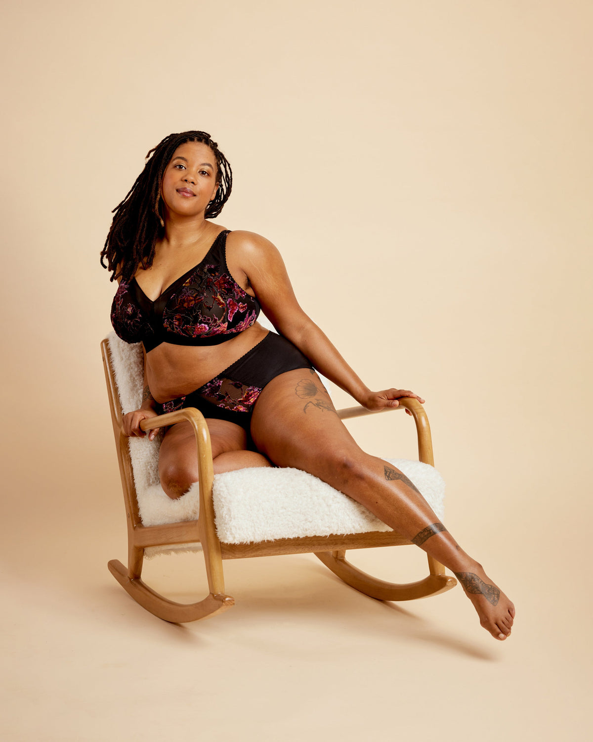 Woman in black lingerie sitting on a rocking chair against a beige background. This bralette is the Loftus Bralette sewing pattern from Cashmerette.