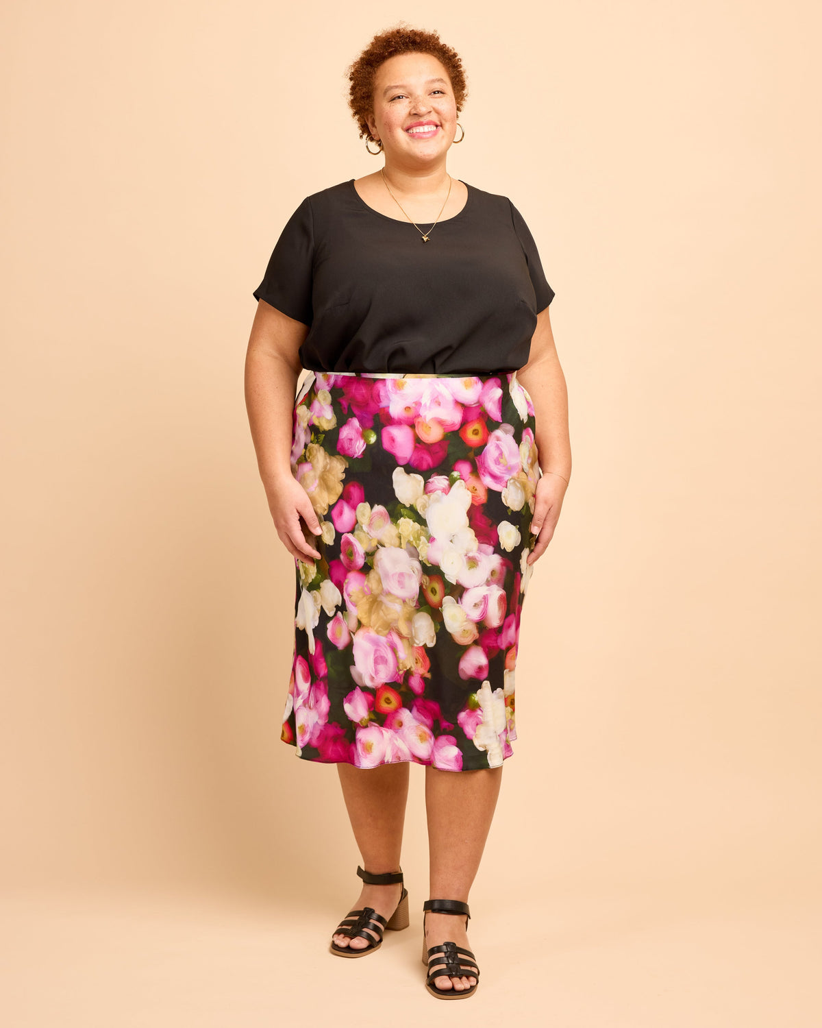Woman wearing a black top and floral skirt on a beige background. This is the Montrose Top sewing pattern from Cashmerette.