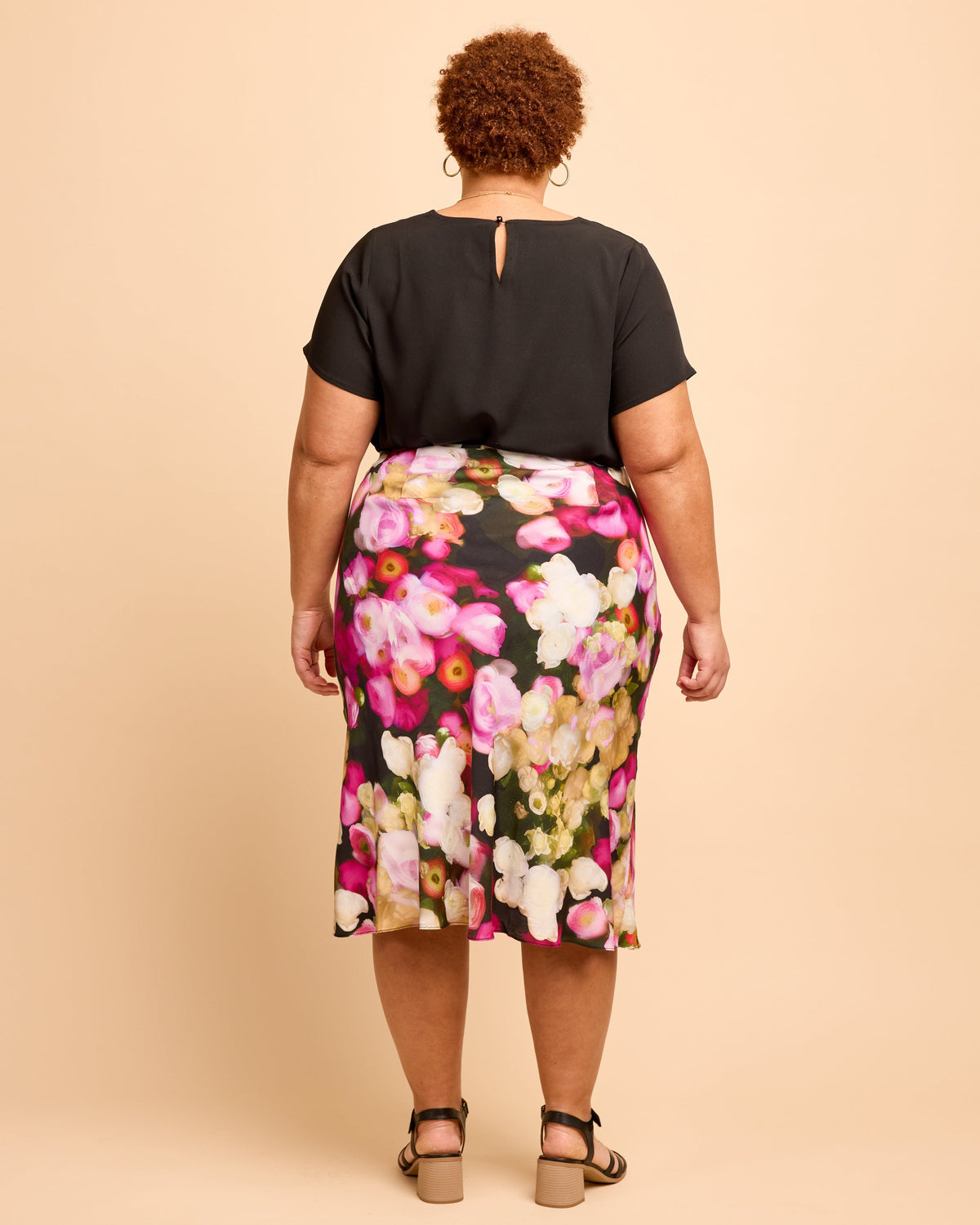 Person wearing a black top and floral skirt on a beige background. This is the Montrose Top sewing pattern from Cashmerette.