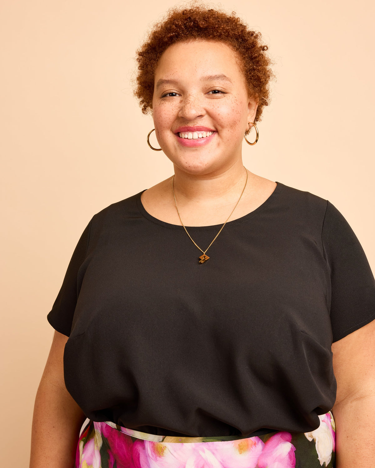 Woman wearing a black top with floral pants against a beige background. This is the Montrose Top sewing pattern from Cashmerette.