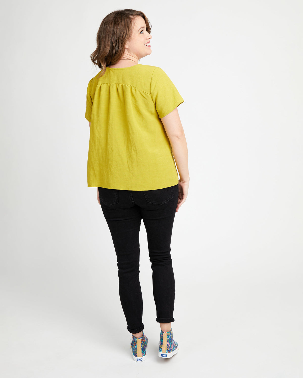 Woman wearing a yellow top and black pants on a white background. This top is the Montrose Top sewing pattern from Cashmerette.