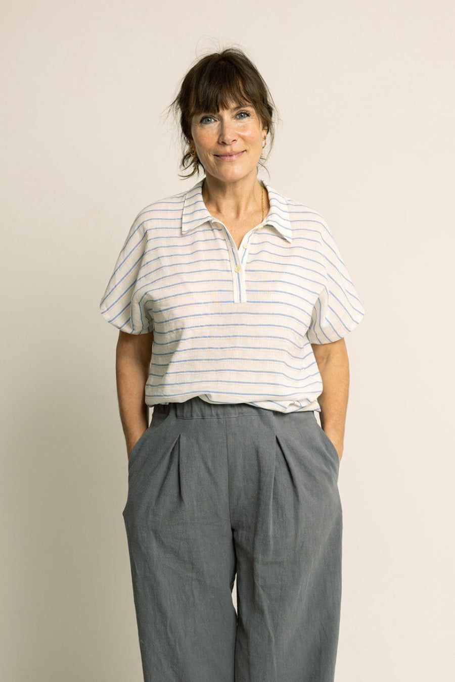 Woman wearing a striped shirt and gray wide-leg pants against a plain background