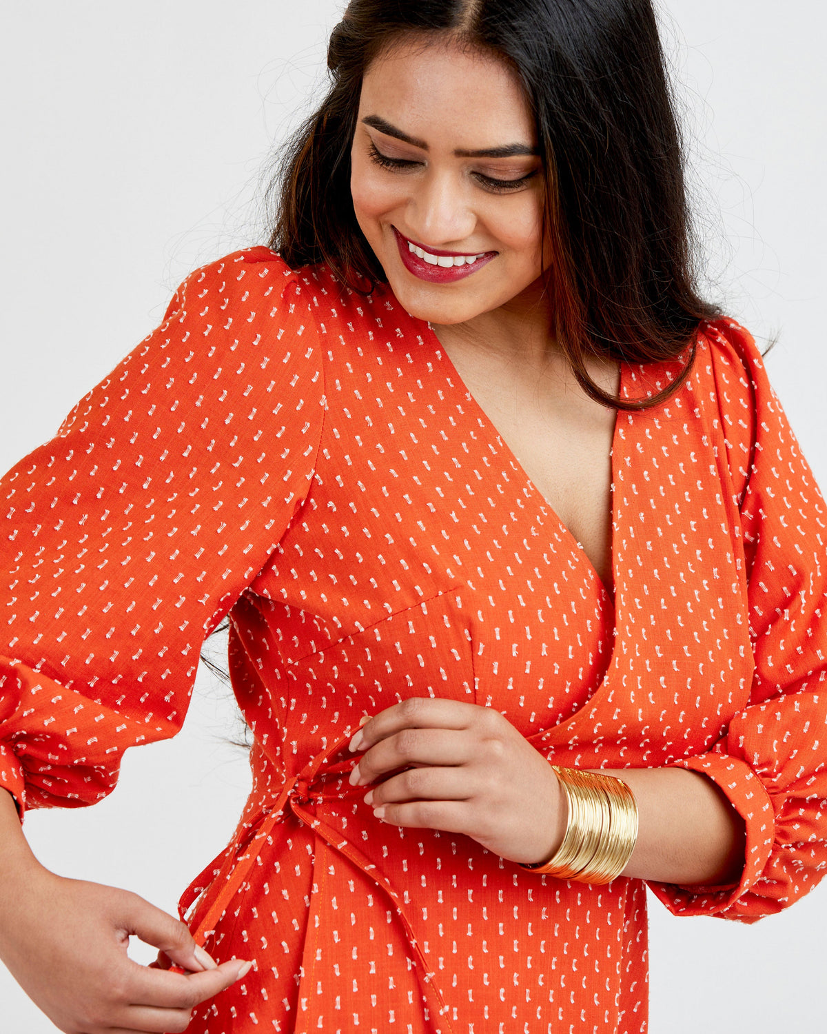 Woman wearing an orange dress with a white pattern on a plain background. This dress is the Roseclair Wrap Dress sewing pattern from Cashmerette.