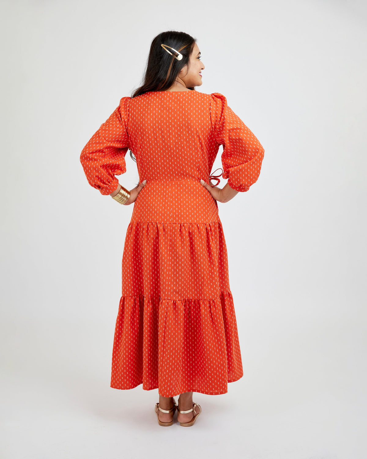 Woman wearing an orange dress with a white background. This dress is the Roseclair Wrap Dress sewing pattern from Cashmerette.