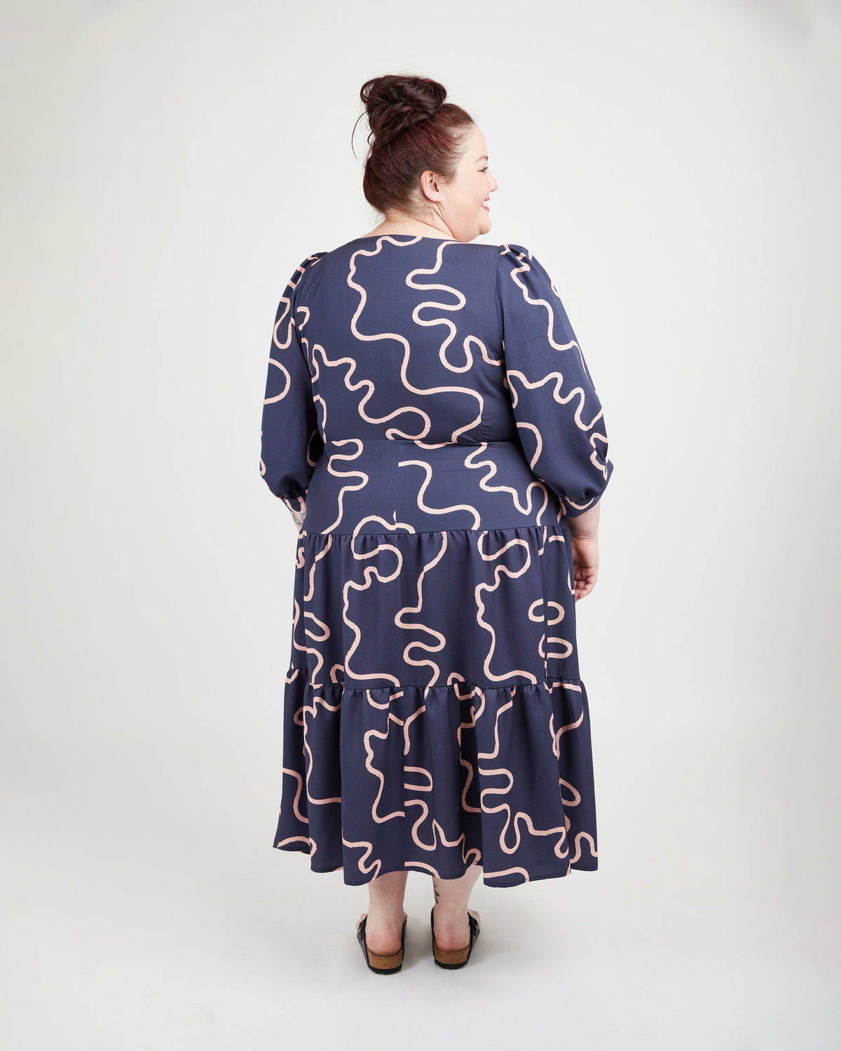 Woman wearing a navy dress with pink wavy patterns on a white background. This dress is the Roseclair Wrap Dress sewing pattern from Cashmerette.