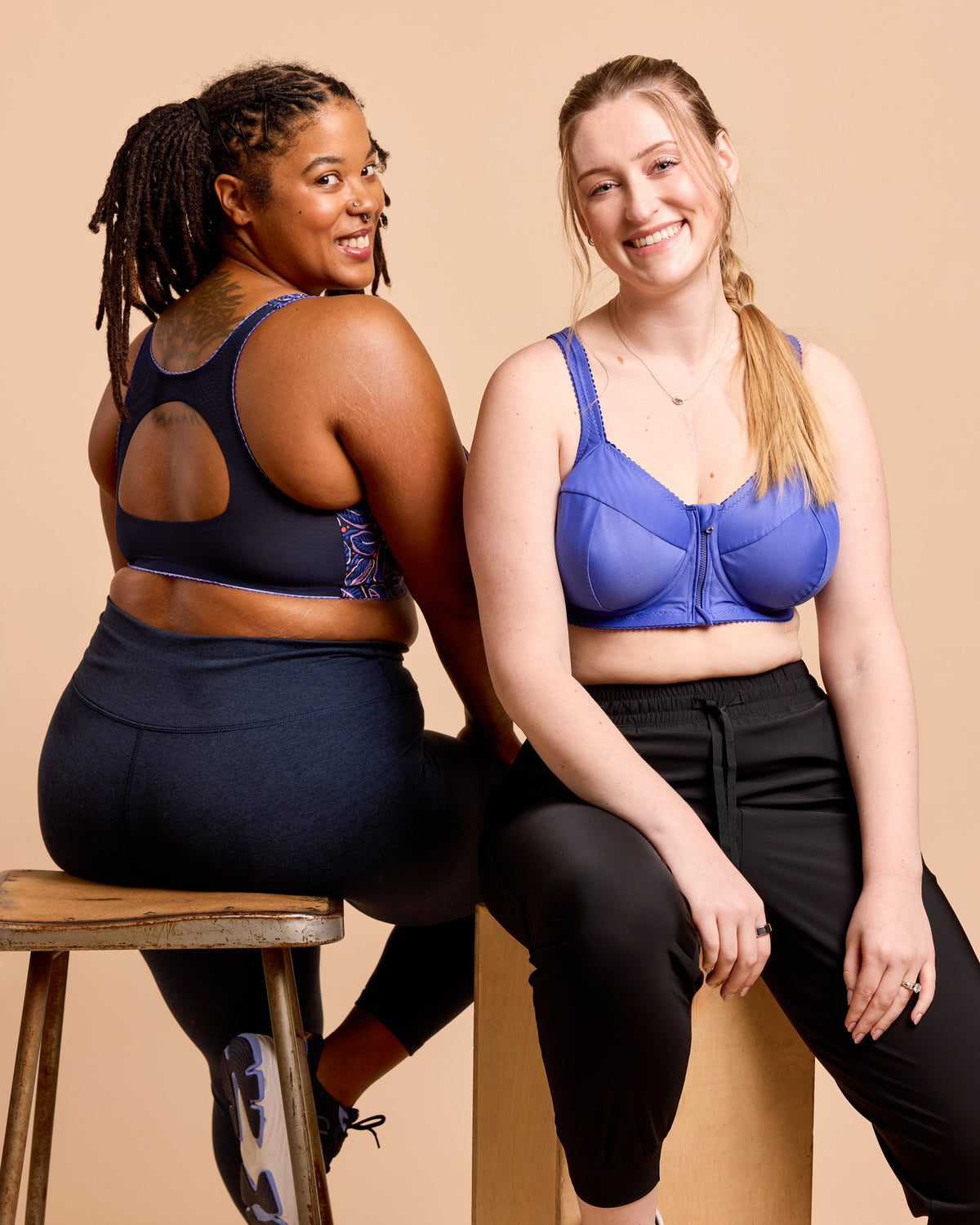 Two women sitting on a stool wearing sports bras and leggings against a beige background. This is the Cashmerette Somerville Sports Bra sewing pattern for big boobs.