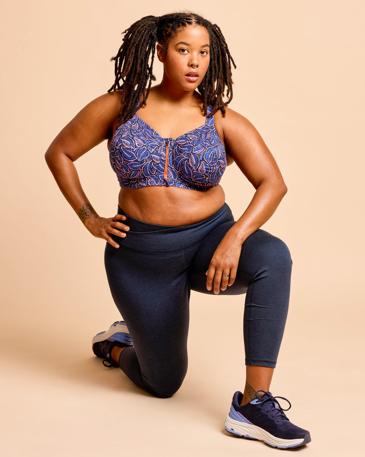 Woman wearing a blue patterned sports bra and navy leggings on a beige background. This is the Cashmerette Somerville Sports Bra sewing pattern for big boobs.