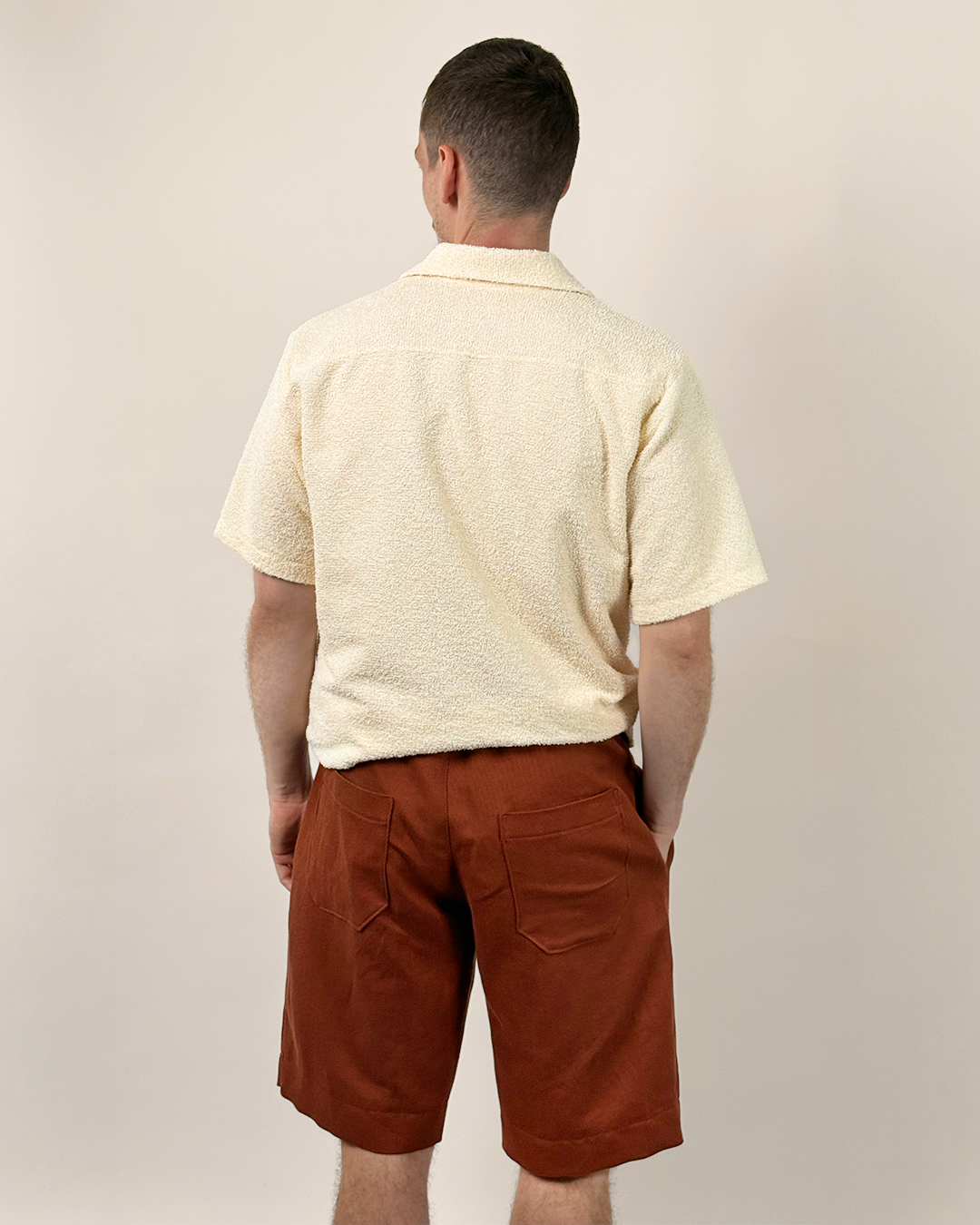 Man wearing a beige shirt and rust-colored shorts against a plain background