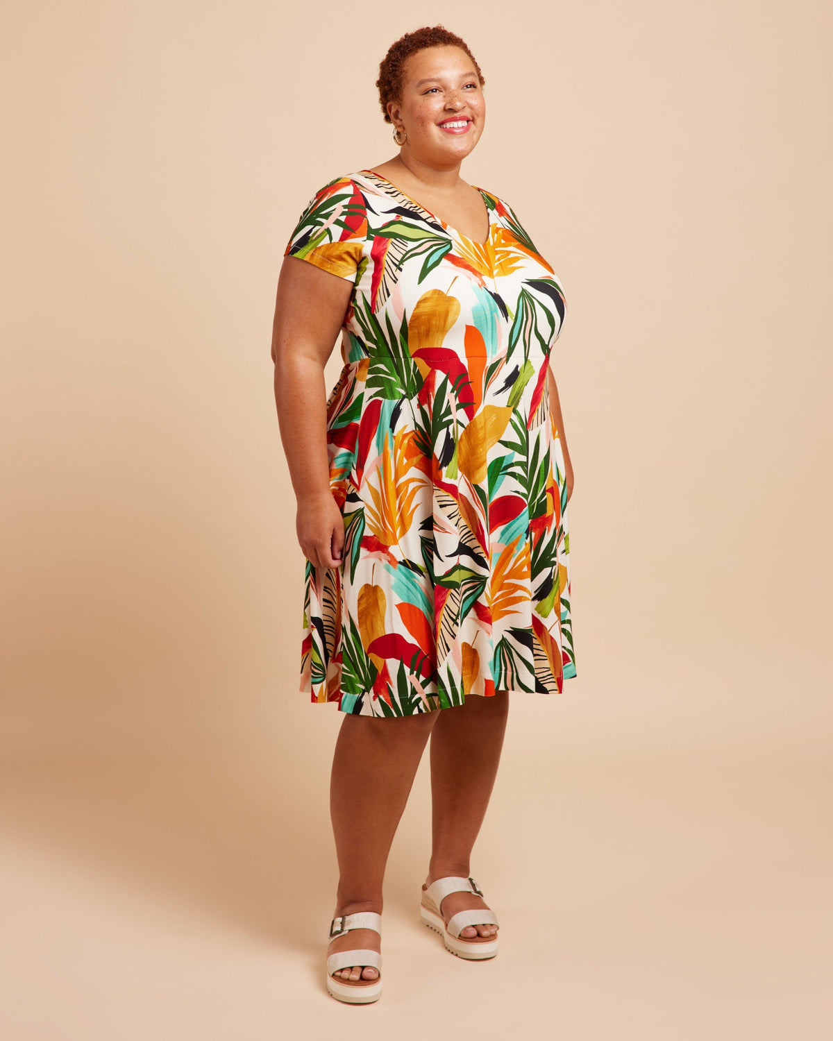 Woman wearing a colorful tropical print dress on a beige background