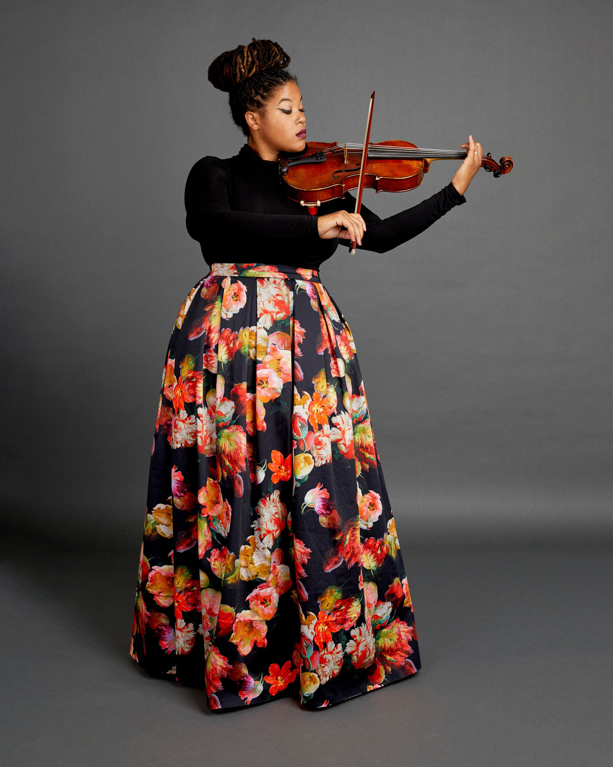 Person playing violin wearing a floral skirt on a gray background. This skirt is the Upton Dress & Skirt sewing pattern from Cashmerette.