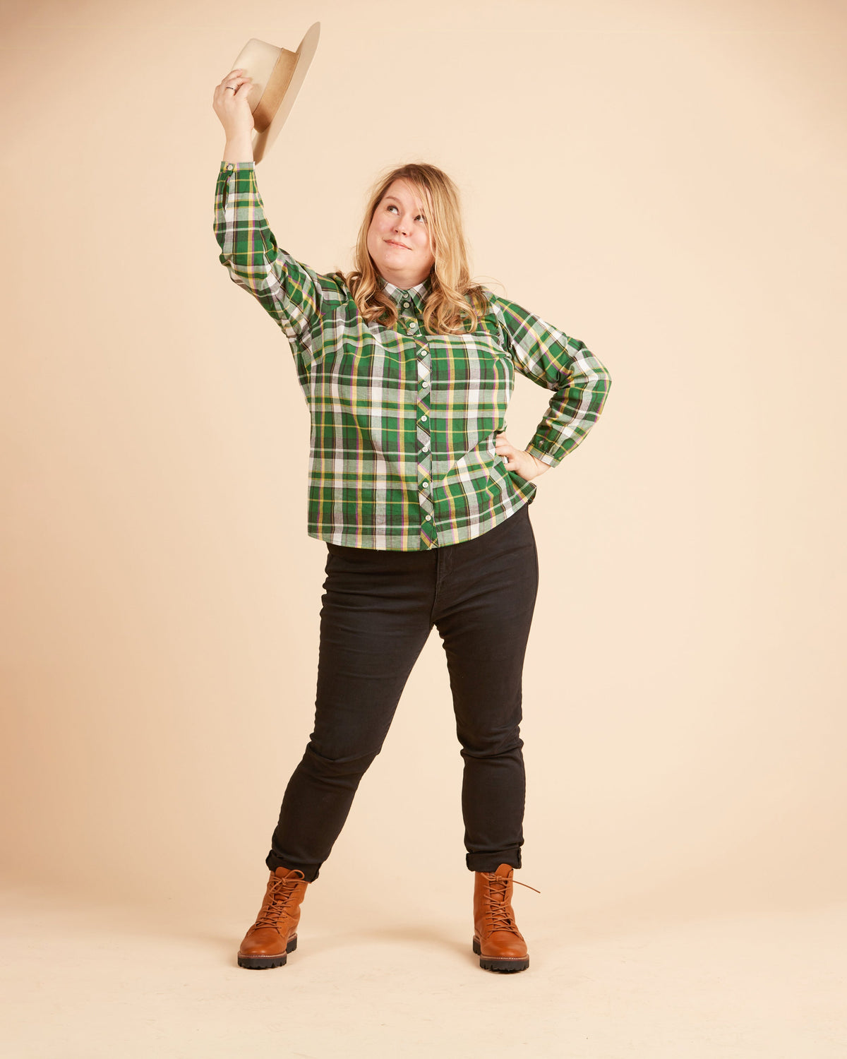 Person wearing a green plaid shirt, black pants, and brown boots against a beige background. This top is the Vernon Shirt sewing pattern from Cashmerette.