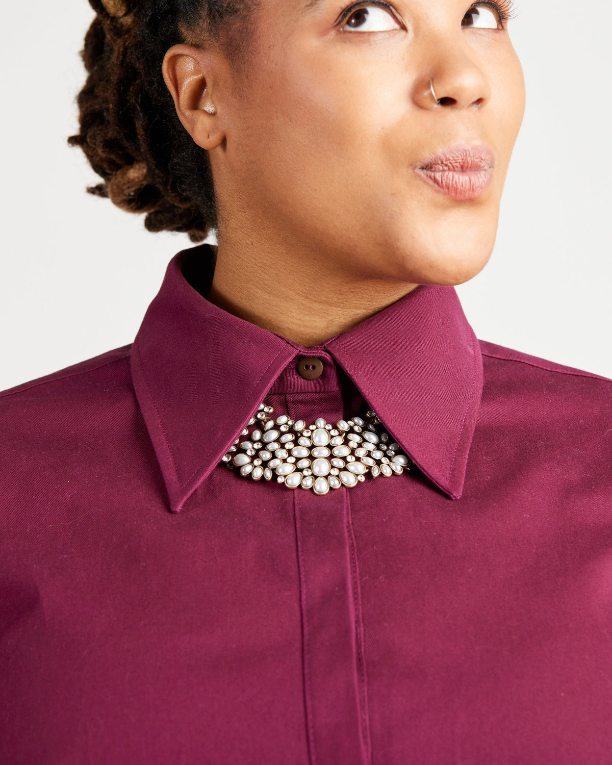 Close-up of a person wearing a purple shirt with a pearl necklace against a white background. This top is the Vernon Shirt sewing pattern from Cashmerette.