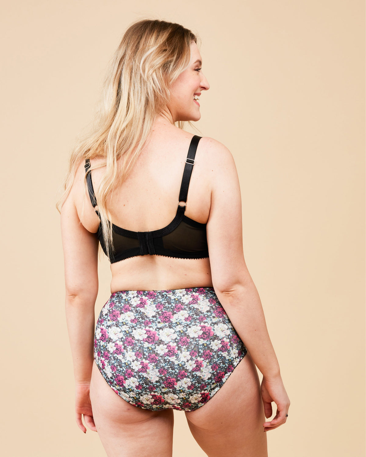 Woman wearing a black bra and floral high-waisted underwear on a beige background. This bra is the Willowdale Bra sewing pattern from Cashmerette.