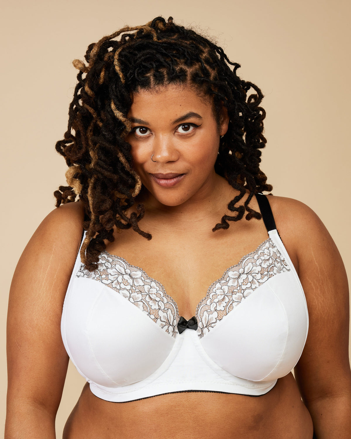 Woman wearing a white bra with lace details against a beige background. This bra is the Willowdale Bra sewing pattern from Cashmerette.